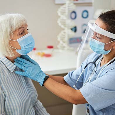 A pediatric nurse in a white coat and mask uses a stethoscope to listen to a young girl's heart, who looks at her with trust and curiosity during a medical check-up in a clinic.