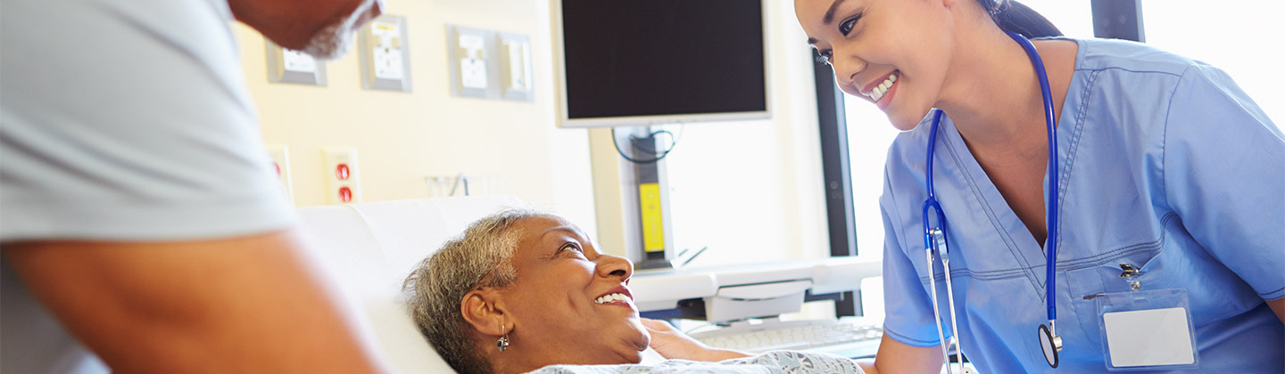 Smiling female medical practitioner attends to smiling patient in hospital bed